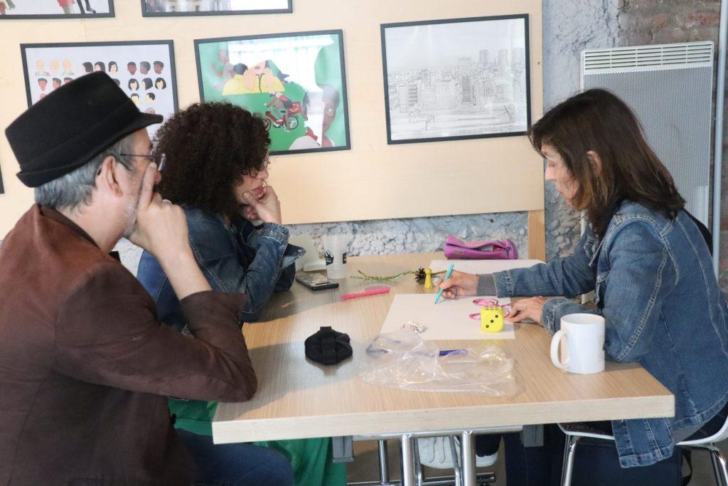 Trois participants refléchissent autour d'objets et feuille posés sur une table.