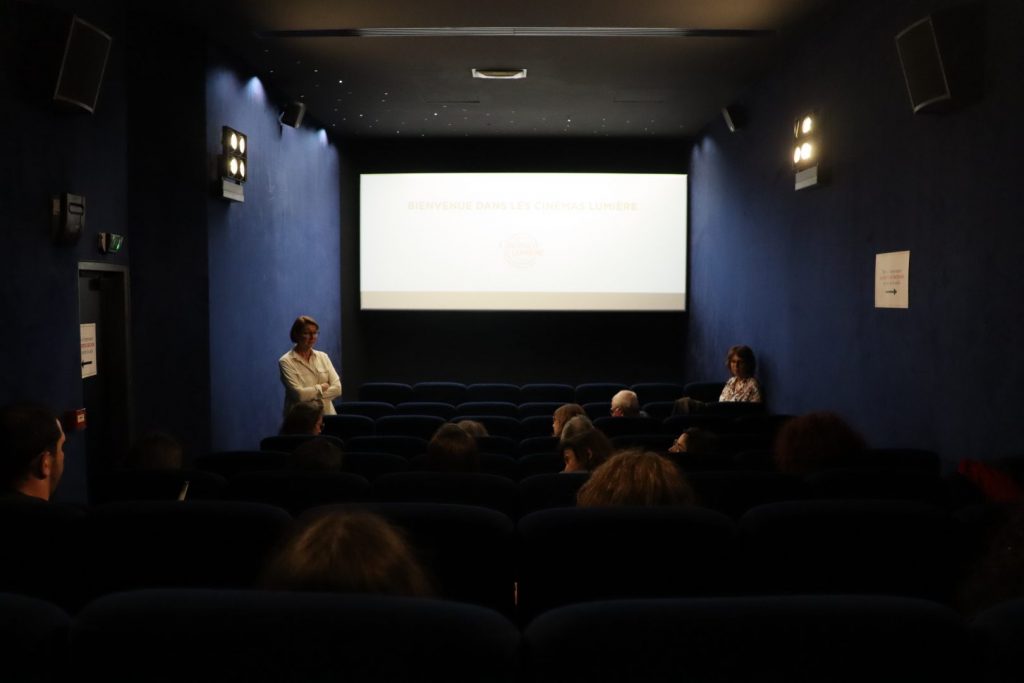 Devant l'écran éclairé, des personnes discutent dans une salle du cinema Lumière Fourmi à Lyon